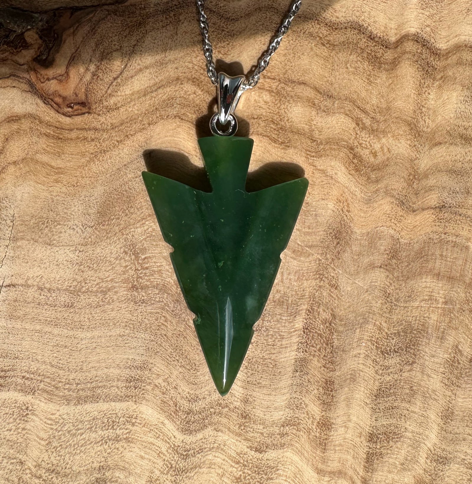Canadian Jade Arrow Pendant on a silver chain against a wood background