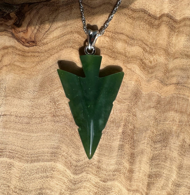 Canadian Jade Arrow Pendant on a silver chain against a wood background
