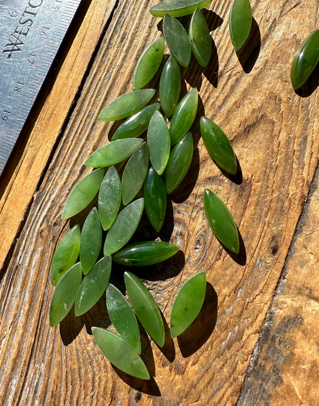 Green marquise cabochons arranged on a wooden surface with a ruler for scale.