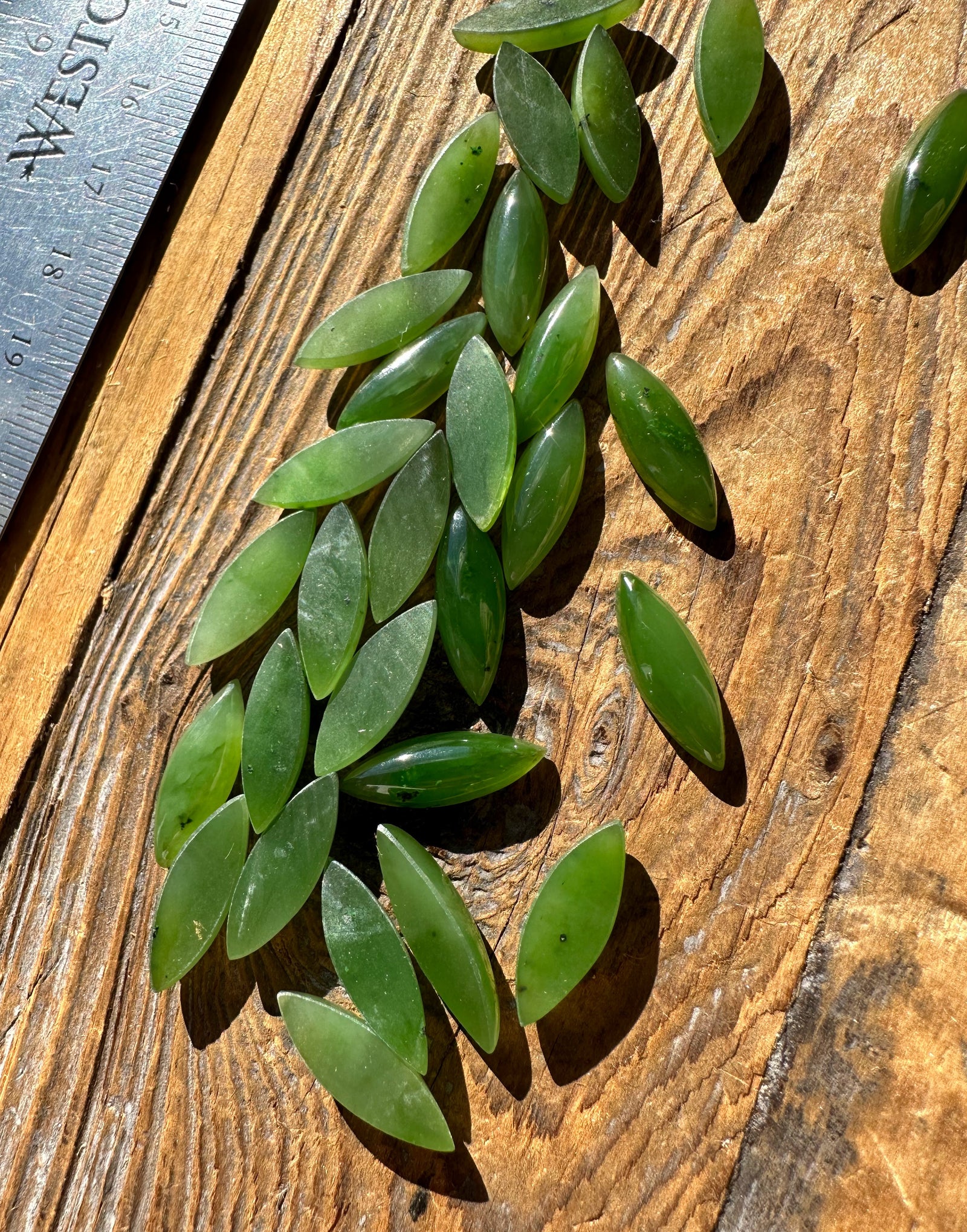 Green marquise cabochons arranged on a wooden surface with a ruler for scale.