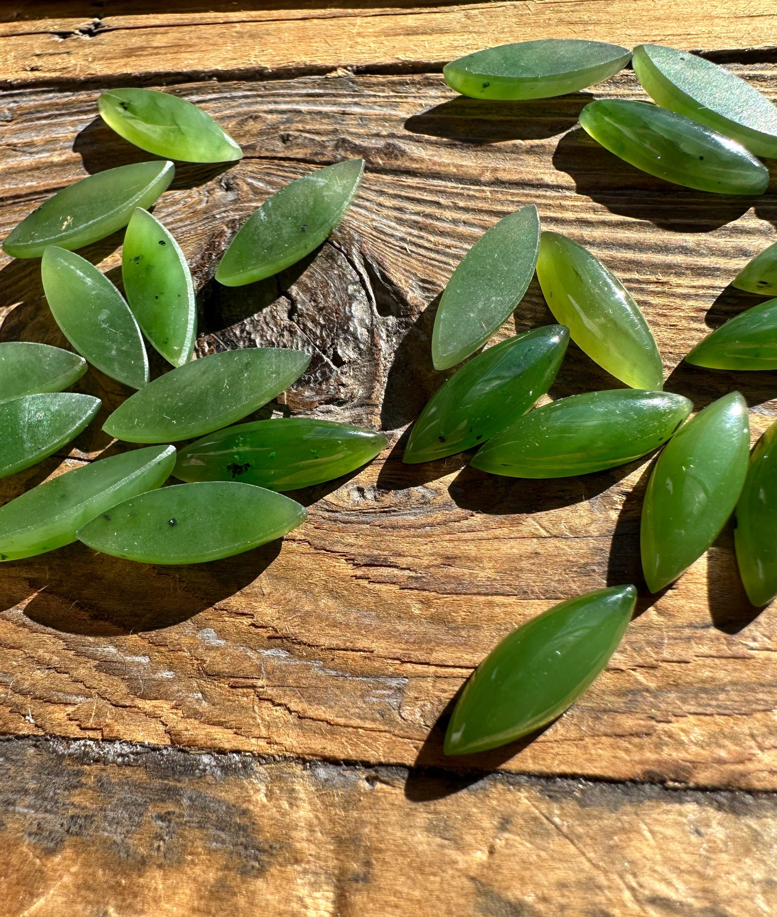 Green marquise cabochons scattered on a rustic wooden surface.