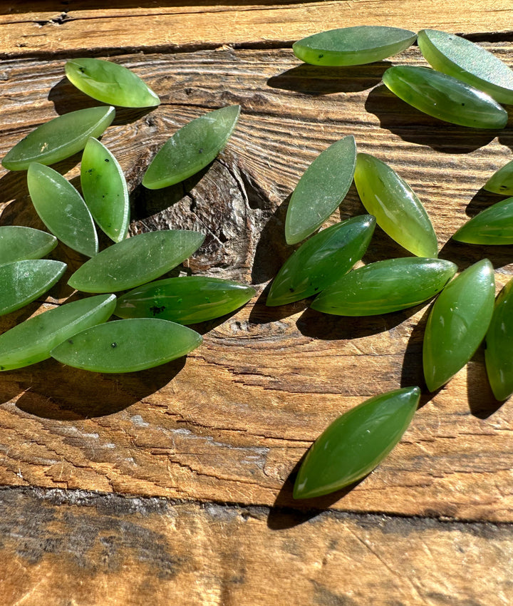 Green marquise cabochons scattered on a rustic wooden surface.