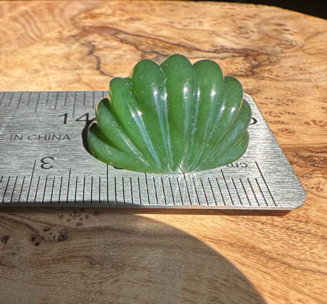 Green jade cabochon on a ruler on a wooden surface