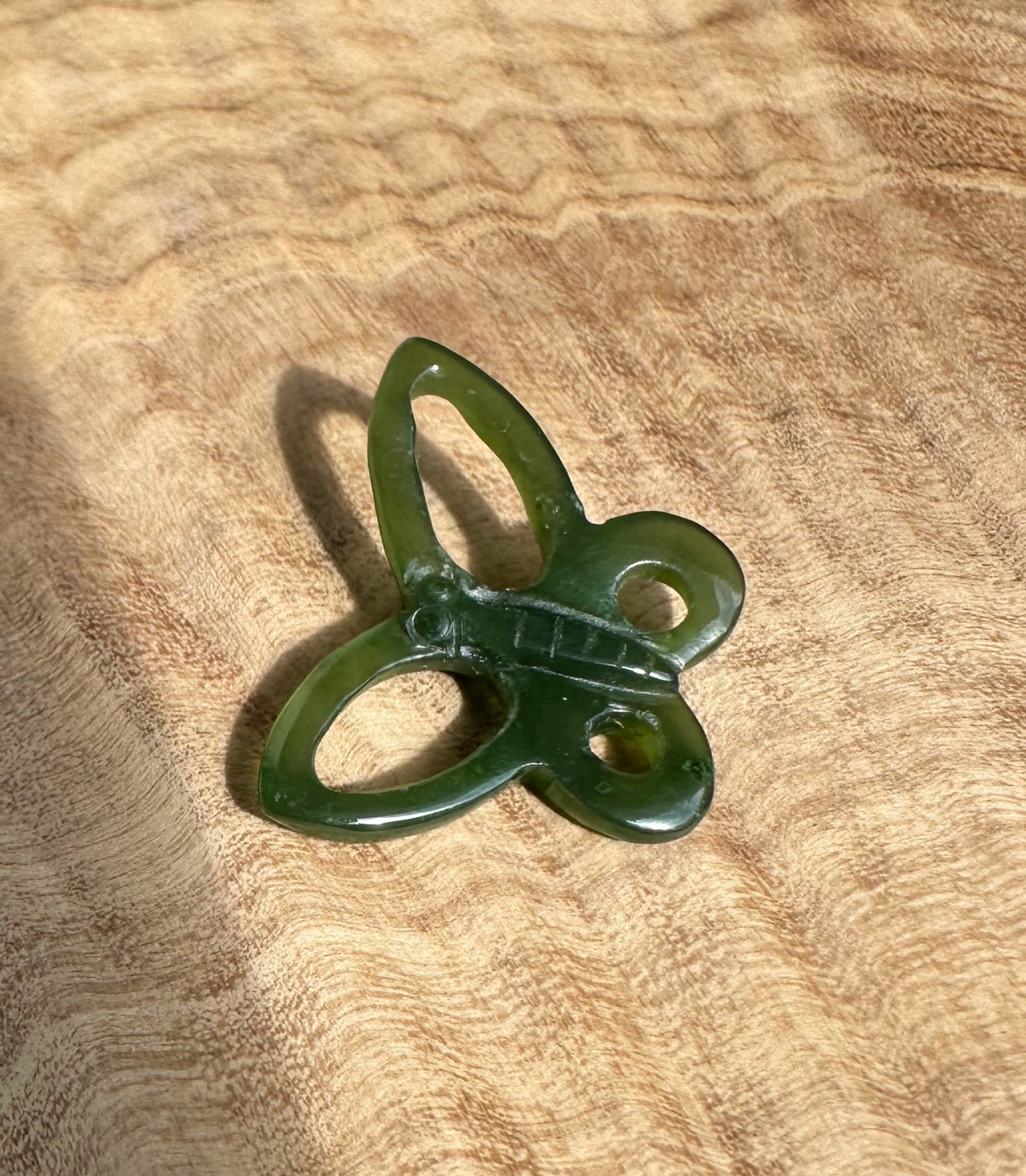 Green butterfly pendant on brown textured fabric background.