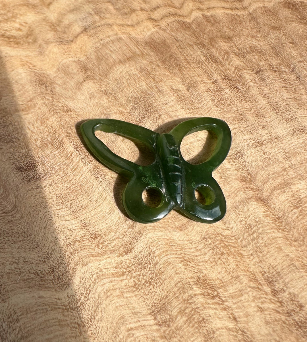 Close up of green butterfly pendant resting on brown textured fabric.