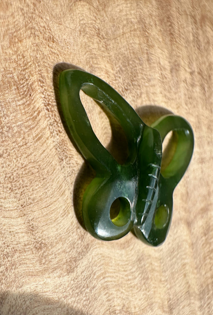 Green jade butterfly pendant with rounded wings resting on a wood surface