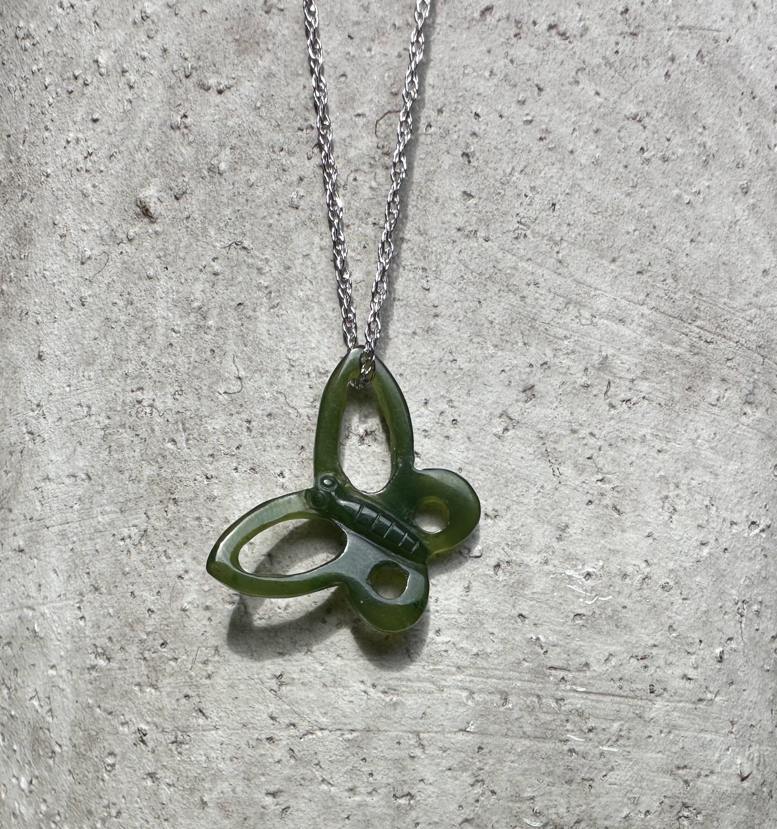 Green butterfly pendant with a silver chain on a textured gray background.