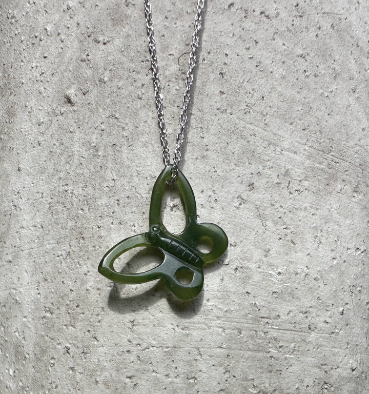 Green butterfly pendant with a silver chain on a textured gray background.