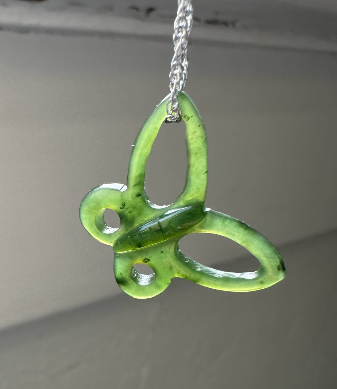 Green butterfly pendant on a silver chain against a neutral background