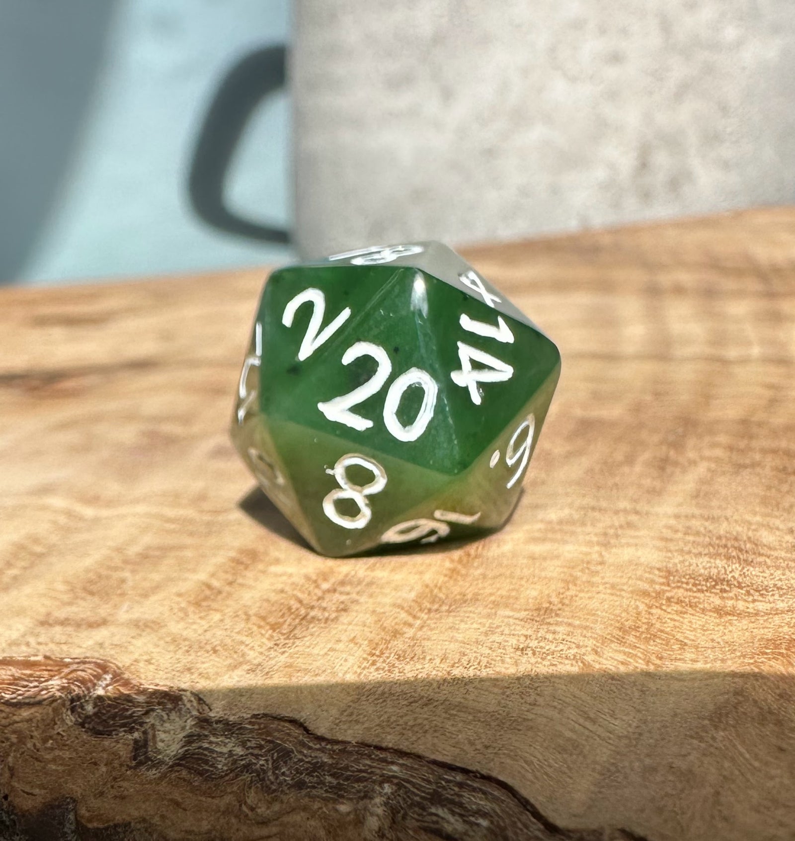 Jade green twenty sided die with white numbers on a wooden surface