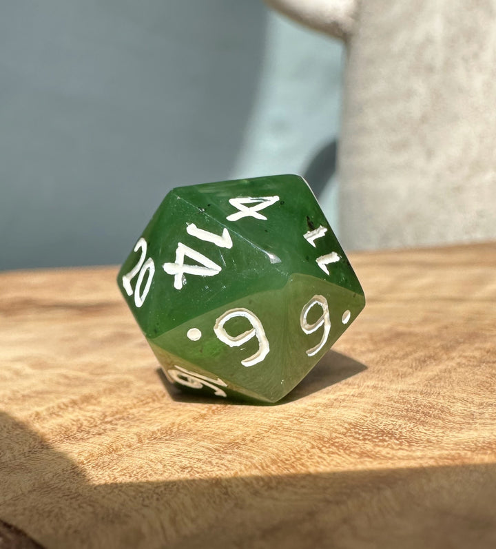 Green jade twenty sided die with white numbers resting on a wooden tabletop