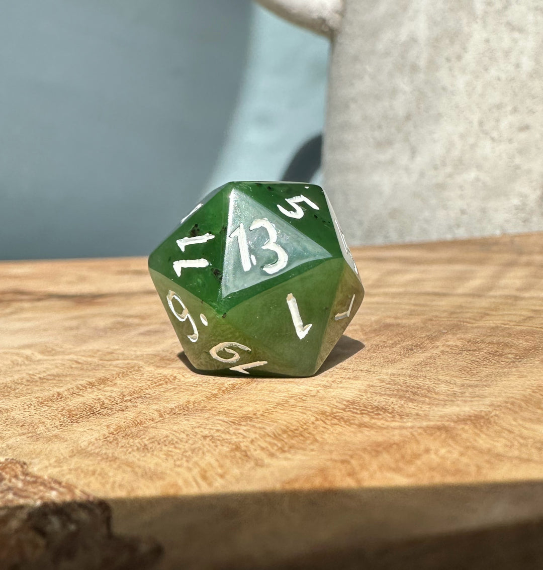 Jade green 20 sided die on wood, displaying the number 13.