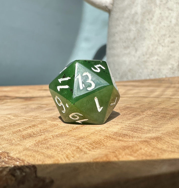 Jade green 20 sided die on wood, displaying the number 13.