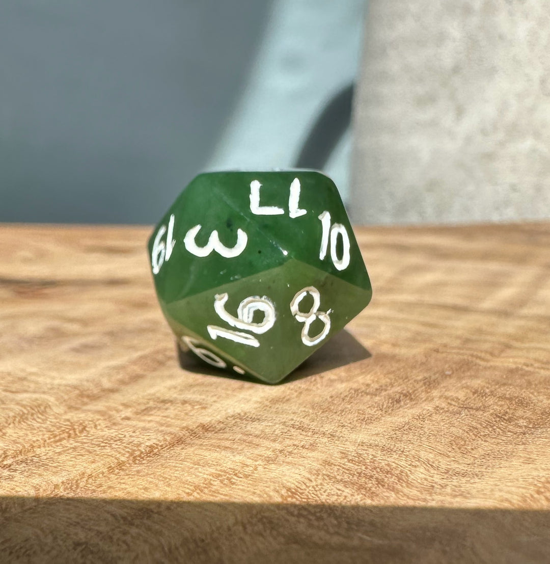 Close up of green jade D20 showing white numerals on a wooden surface