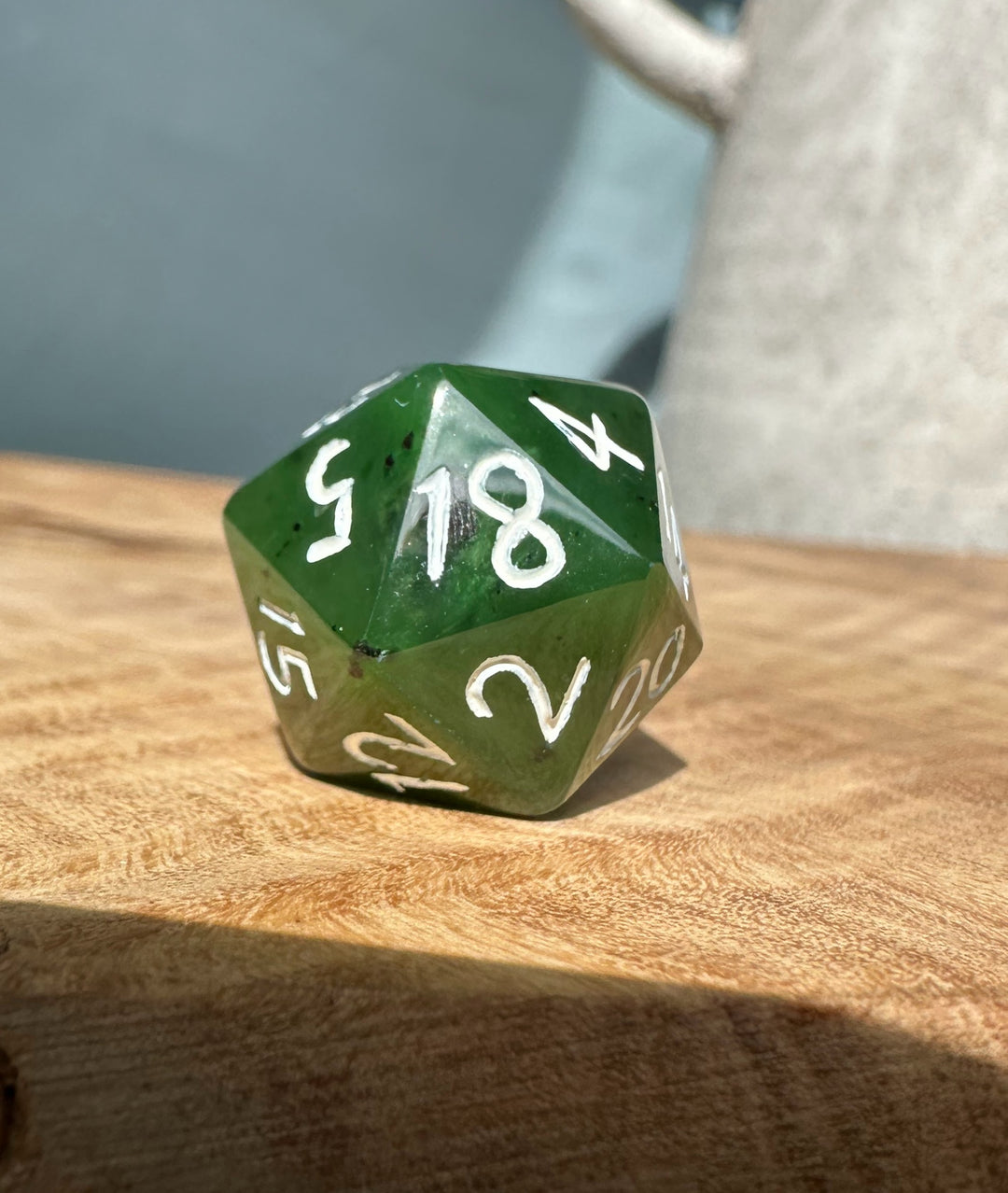 Jade green 20 sided die with white numerals resting on a wooden surface.