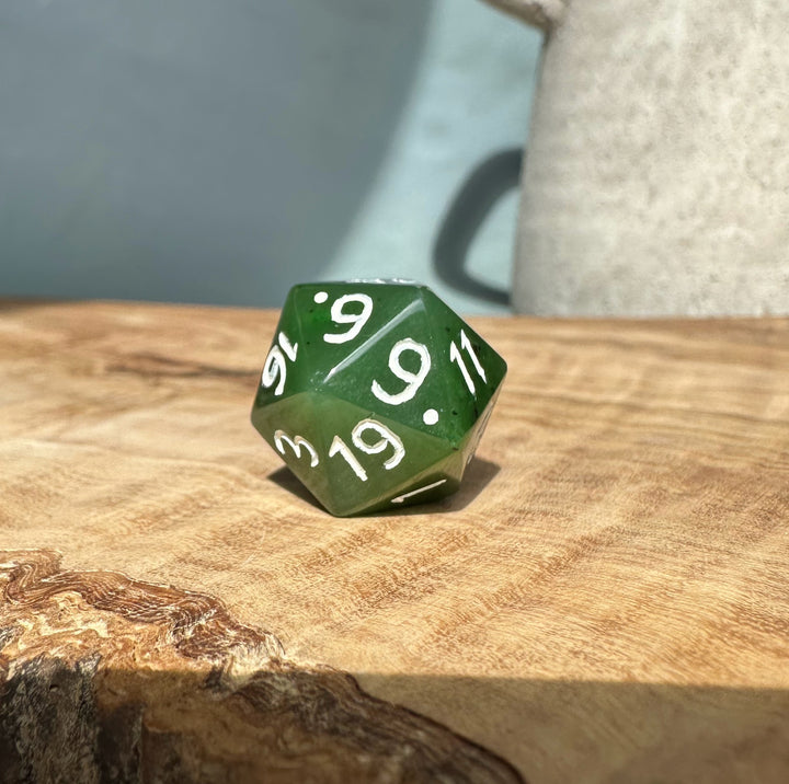 Green jade 20 sided die on a wood surface with white numbers visible