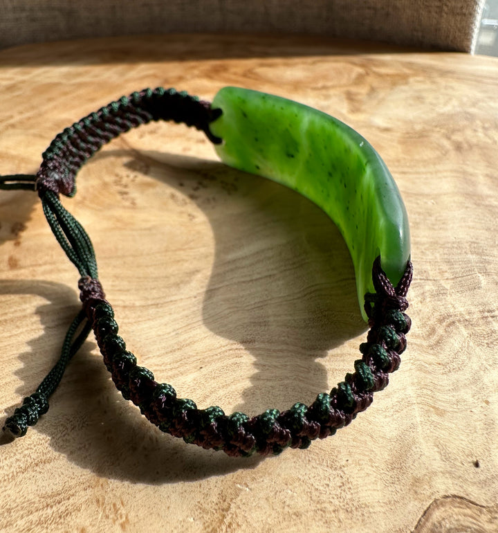 Close up of a green curved jade bracelet showing the braided cord on wood surface