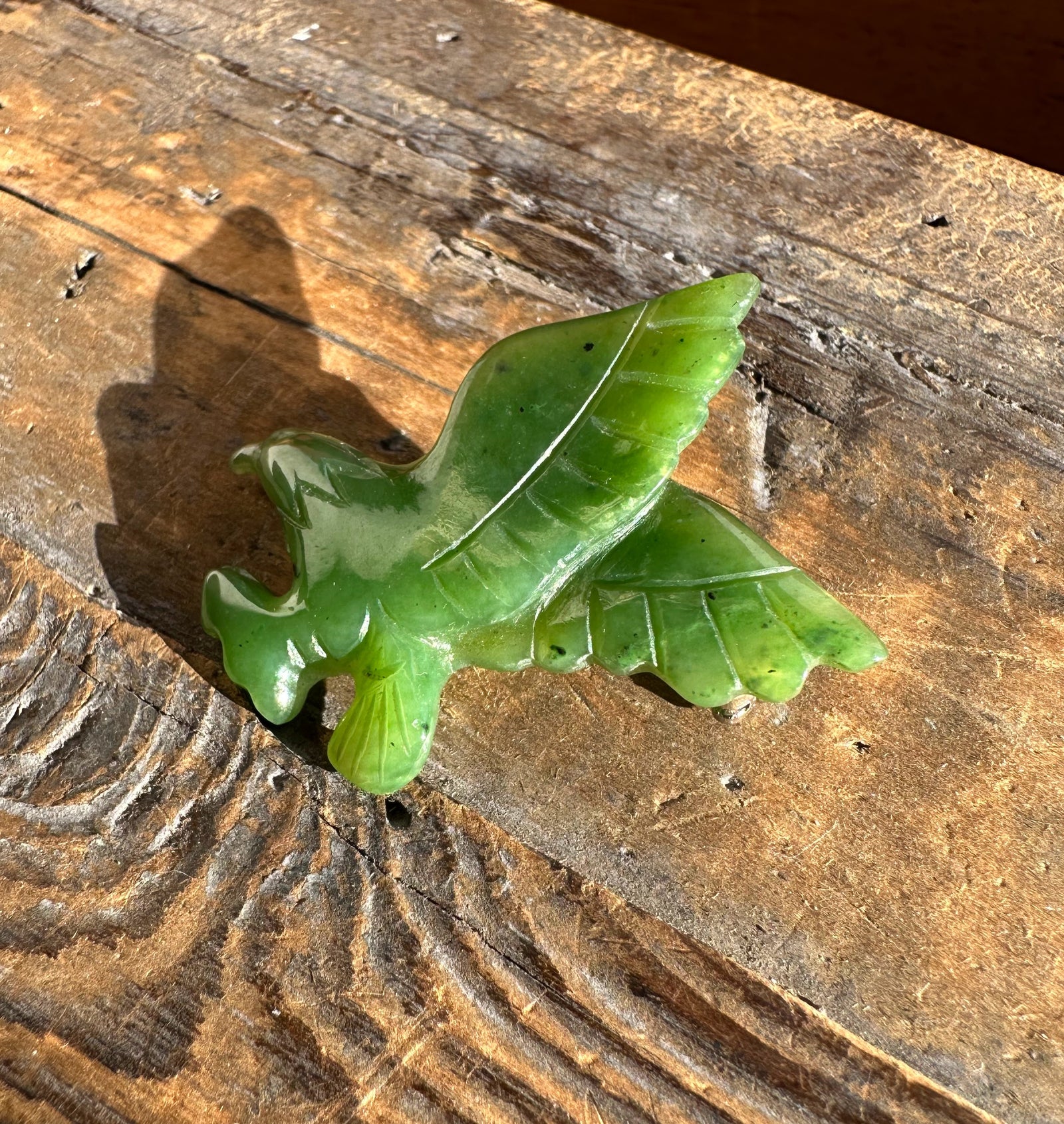 Green jade eagle brooch with carved wings resting on a weathered wooden surface