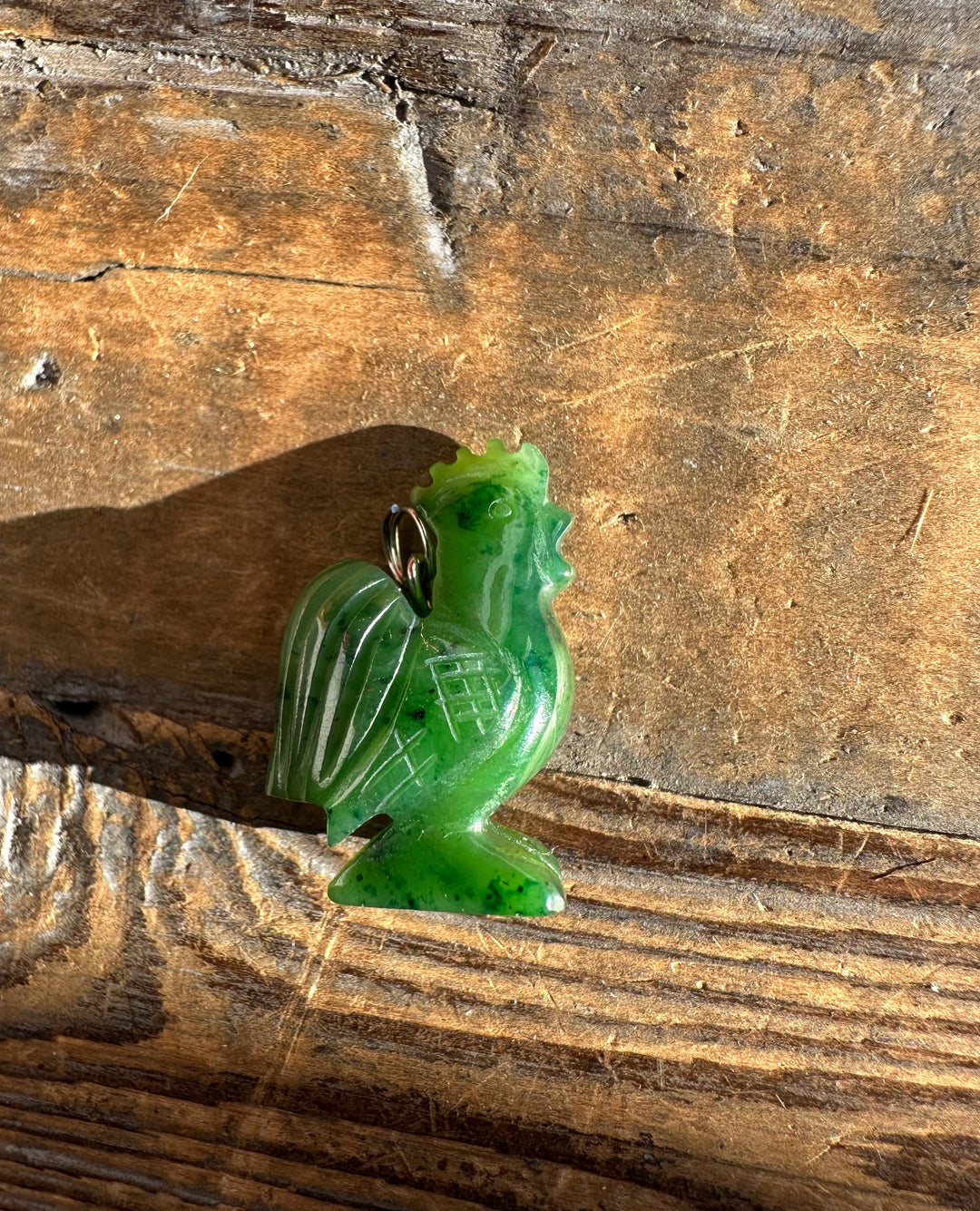 1 inch green jade rooster pendant with a metal ring bail on rustic wood