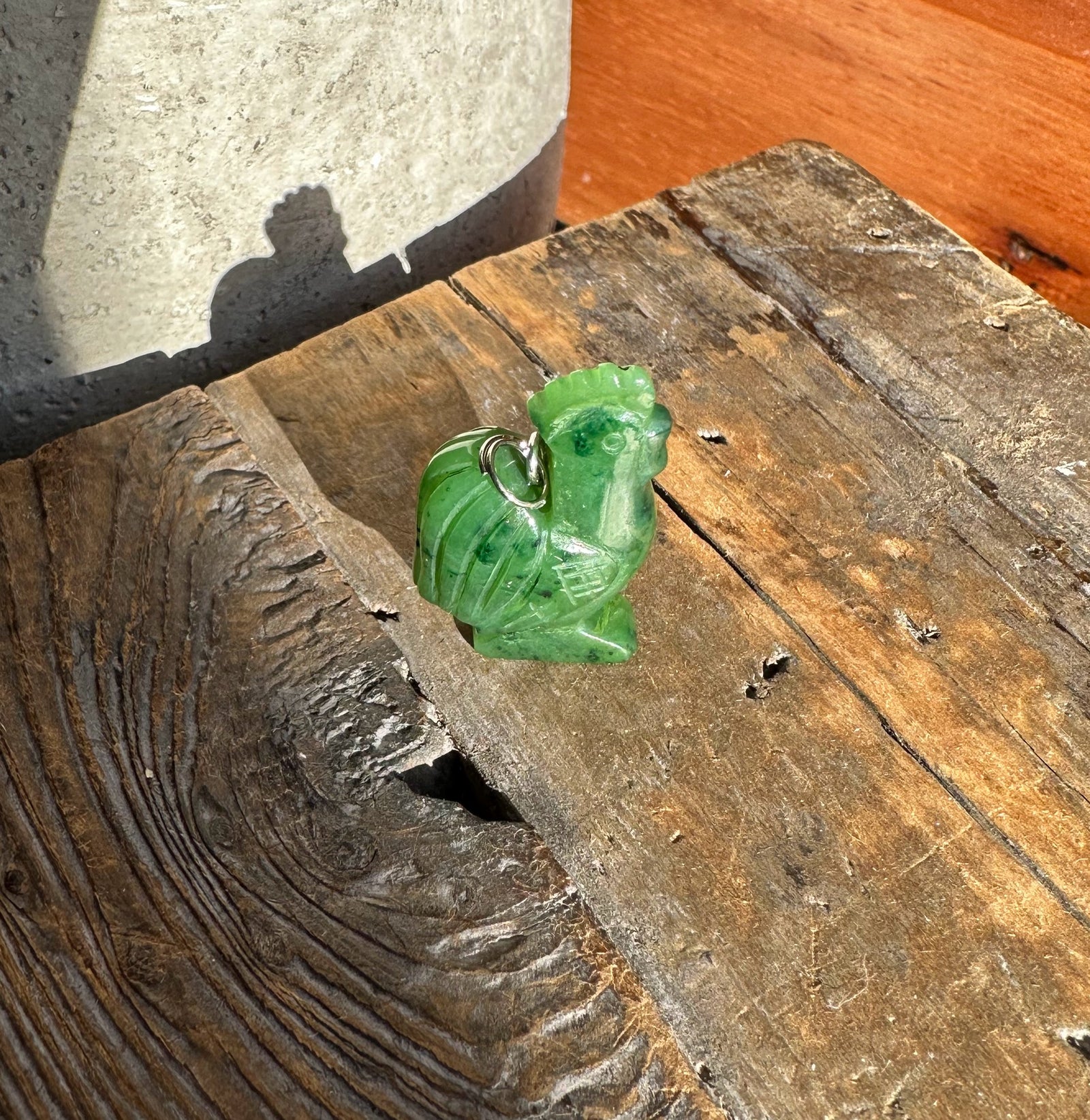 Green jade rooster pendant on a silver chain against weathered wood