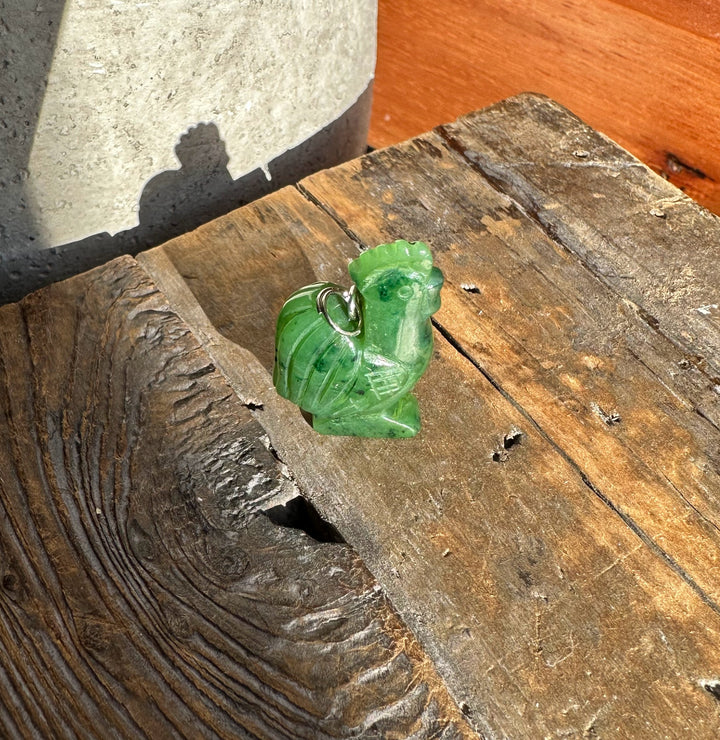 Green jade rooster pendant on a silver chain against weathered wood