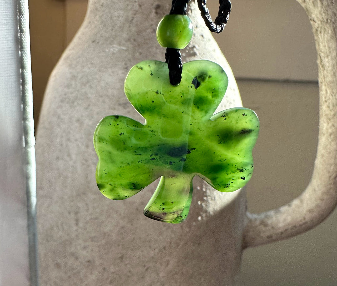 Close-up of a green jade three leaf clover pendant on a black cord