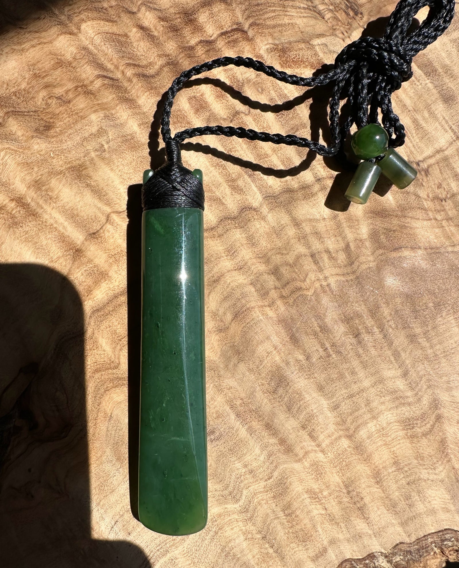 Green jade pendant on a black cord against a wooden background