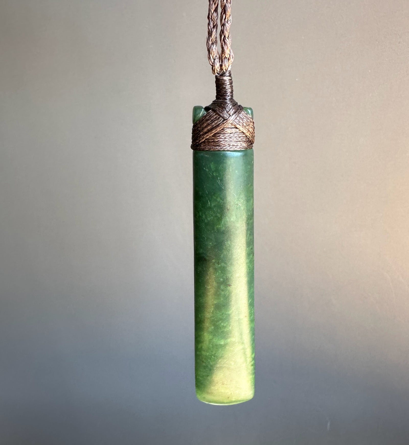 Green pendant necklace with braided cord on a gradient background