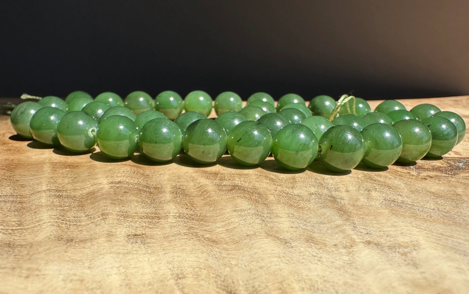 Green jade 10mm beads on a wooden surface with a dark background