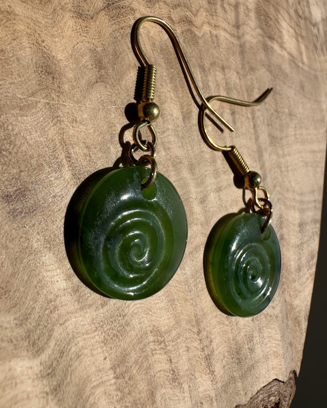 Polar Koru earrings featuring green spiral discs and brass ear wires on a wooden surface