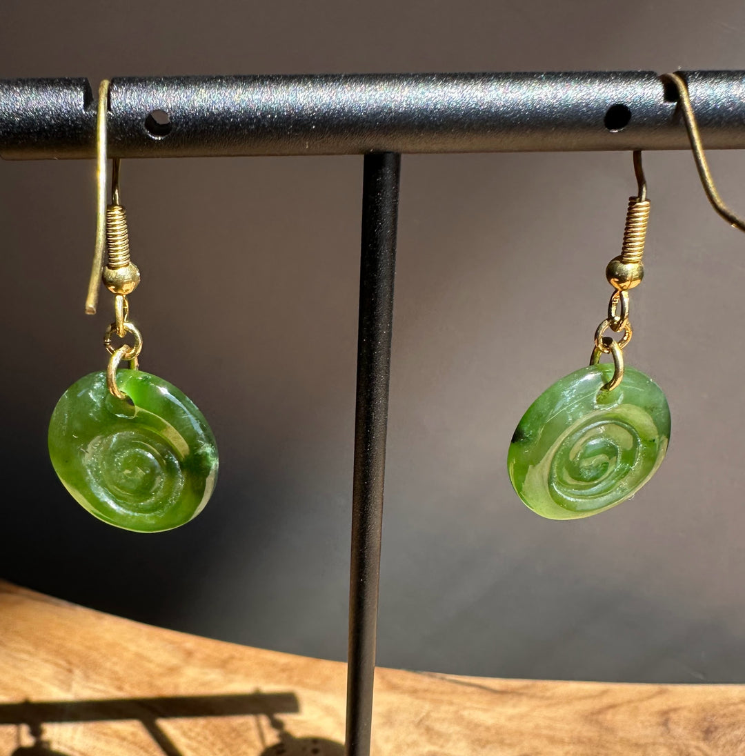 Green spiral earrings on a black stand with a wooden surface