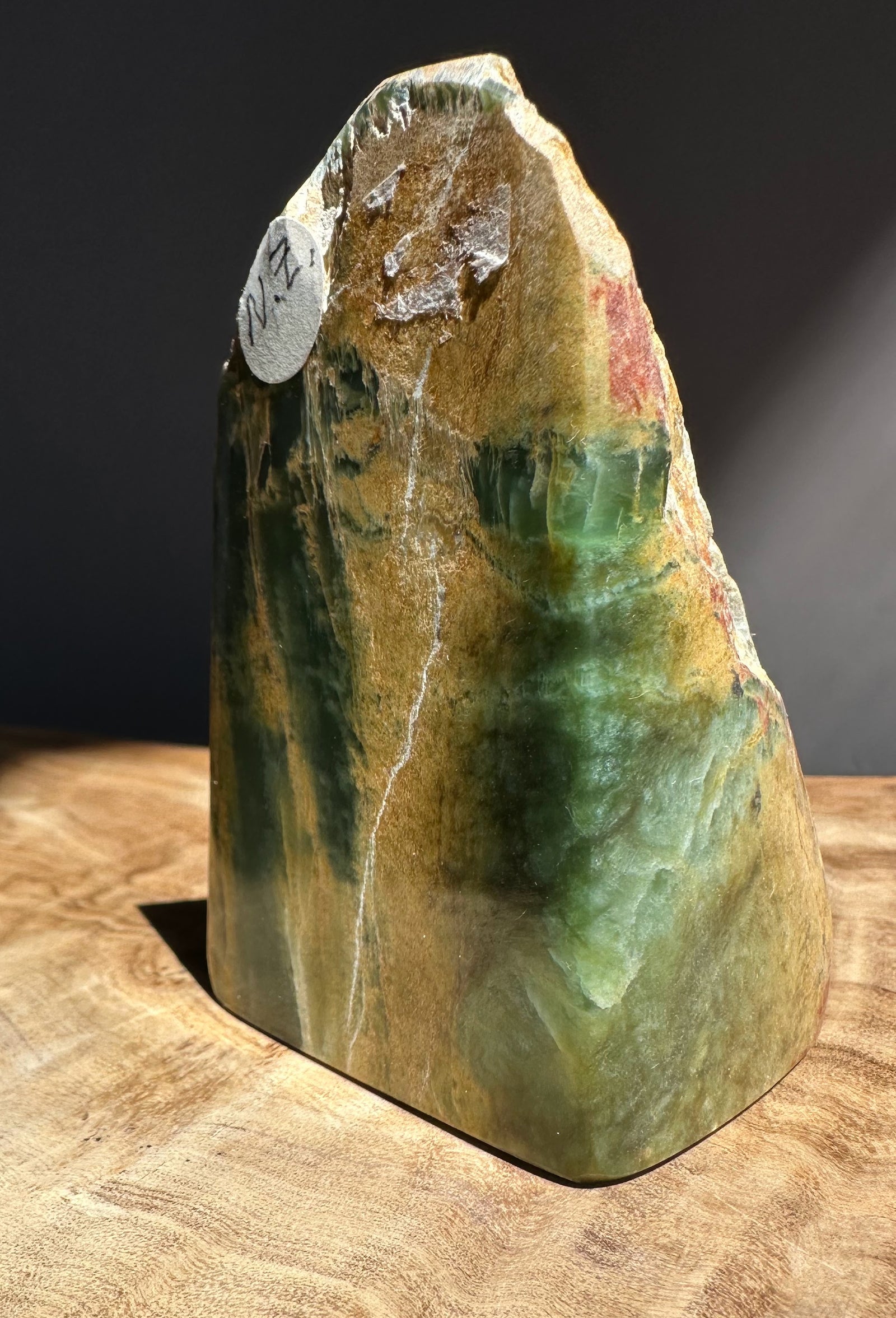 Polished jade with green and brown hues on a wooden surface