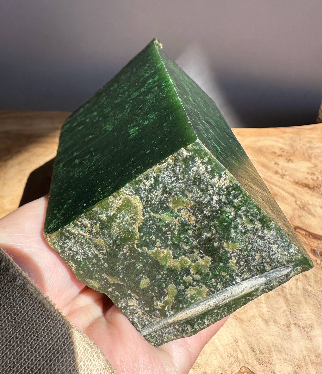 Green jade rough held in a hand with a wooden surface in the background