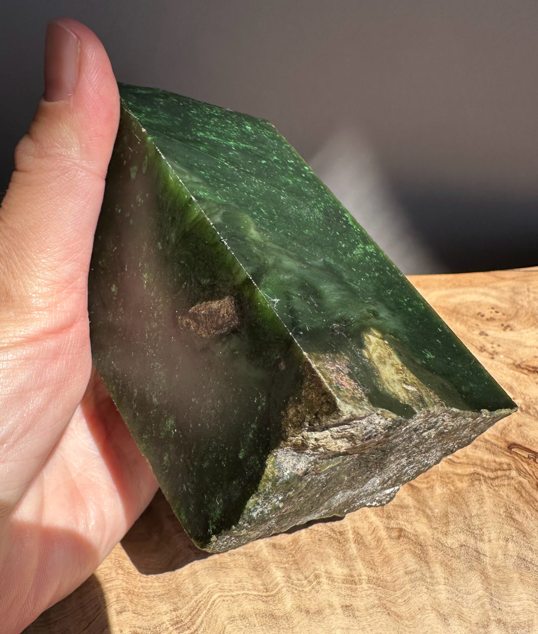Hand holding a green jade on a wooden surface
