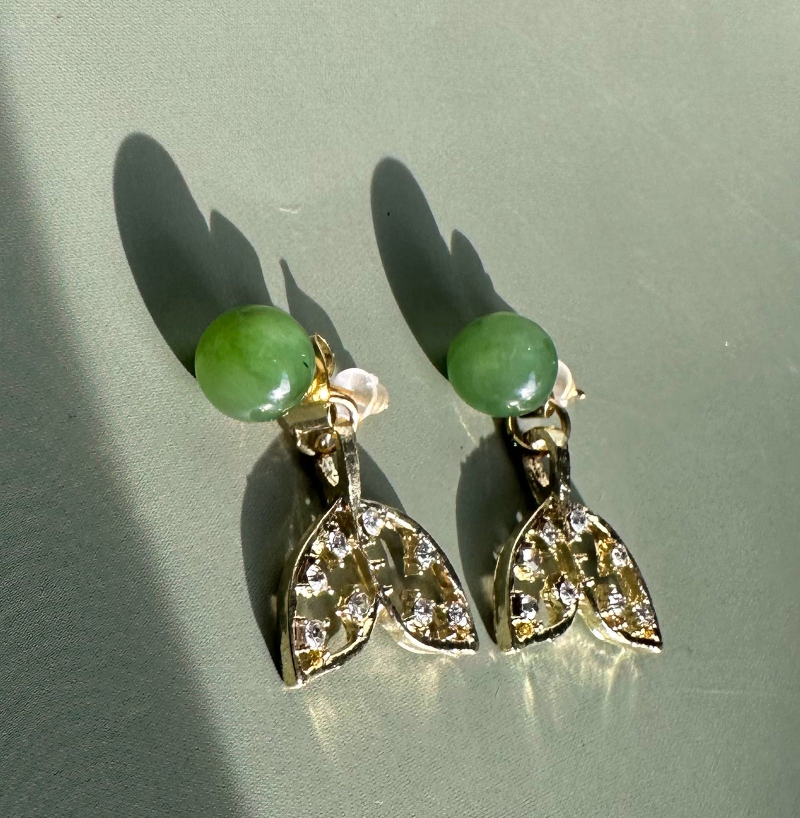 Whale tail earrings with green beads on top and crystal studded silver tails.