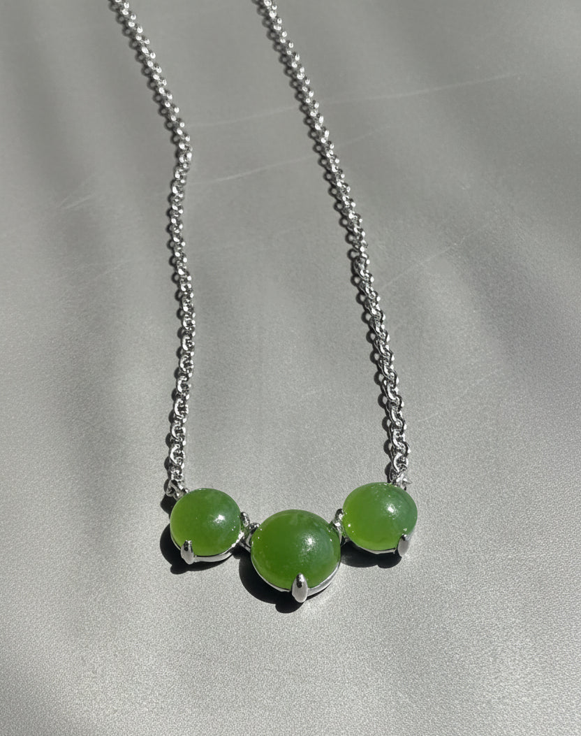 Necklace with three green beads on a silver chain against a gray background