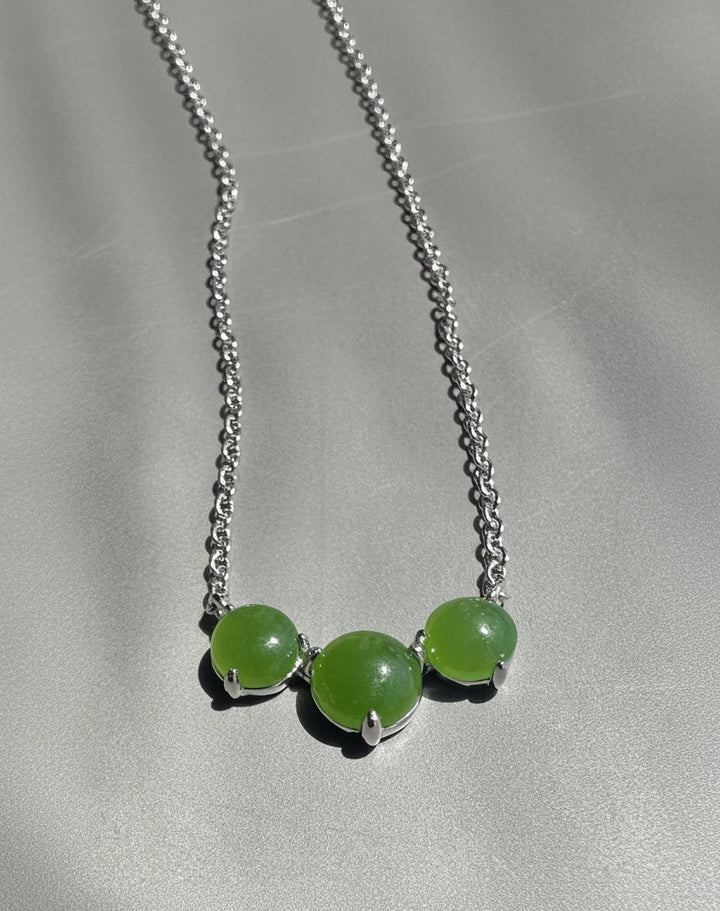 Necklace with three green beads on a silver chain against a gray background