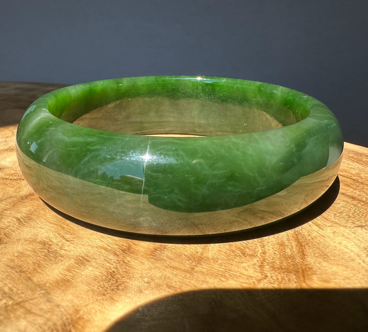 Green jade bangle on a wooden surface with a dark background
