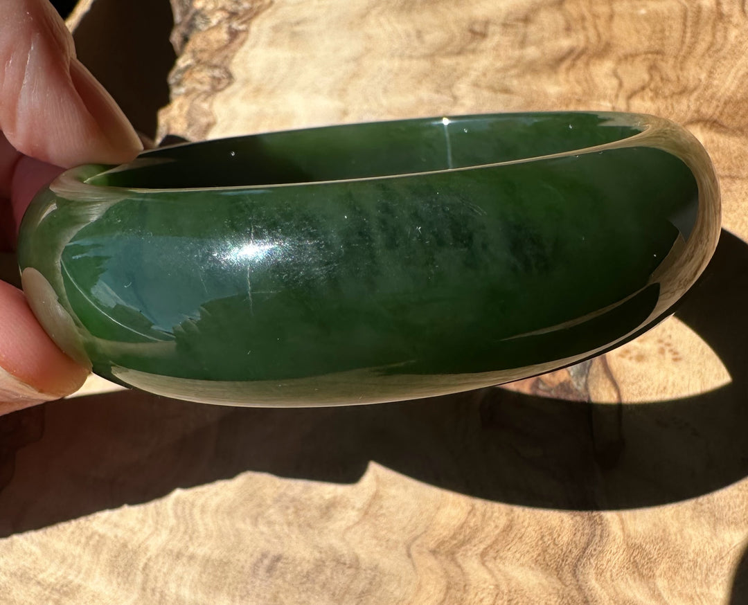 Green bangle held by a hand on a wooden surface