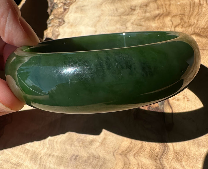 Green bangle held by a hand on a wooden surface