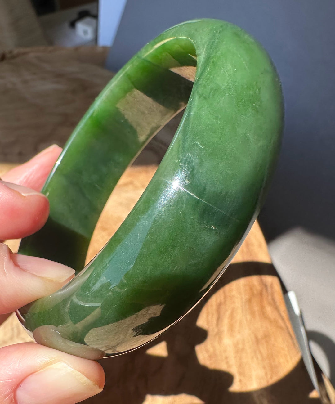 Green jade bracelet held by a hand on a wooden surface