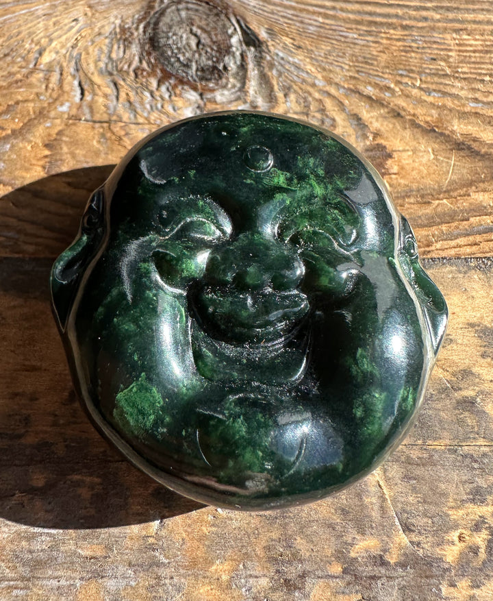 Dark green Canadian jade round double sided Happy Buddha head pendant with carved face resting on wood