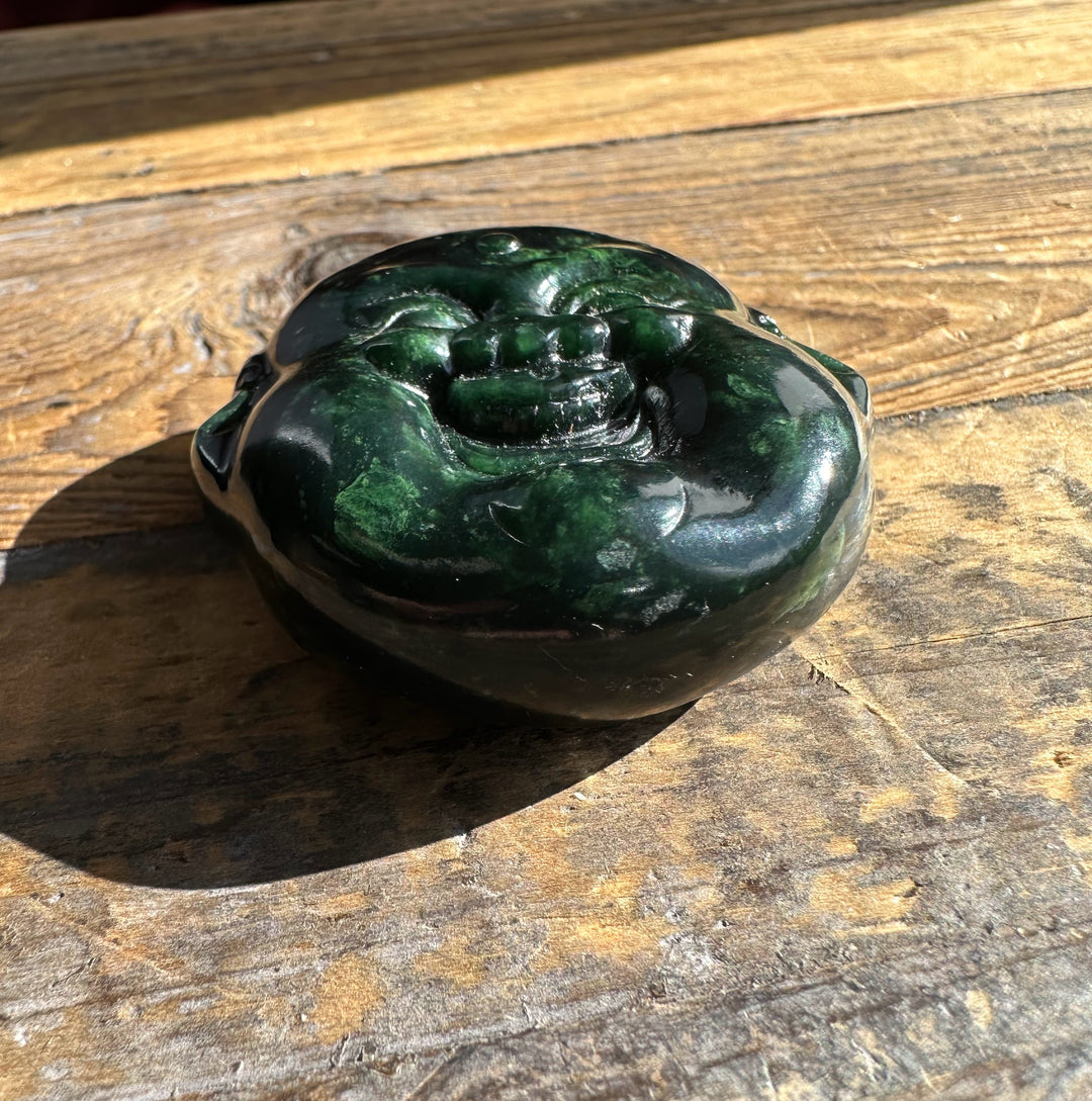 Close up of a 50mm dark jade Happy Buddha head on a wooden surface showing a glossy smiling face