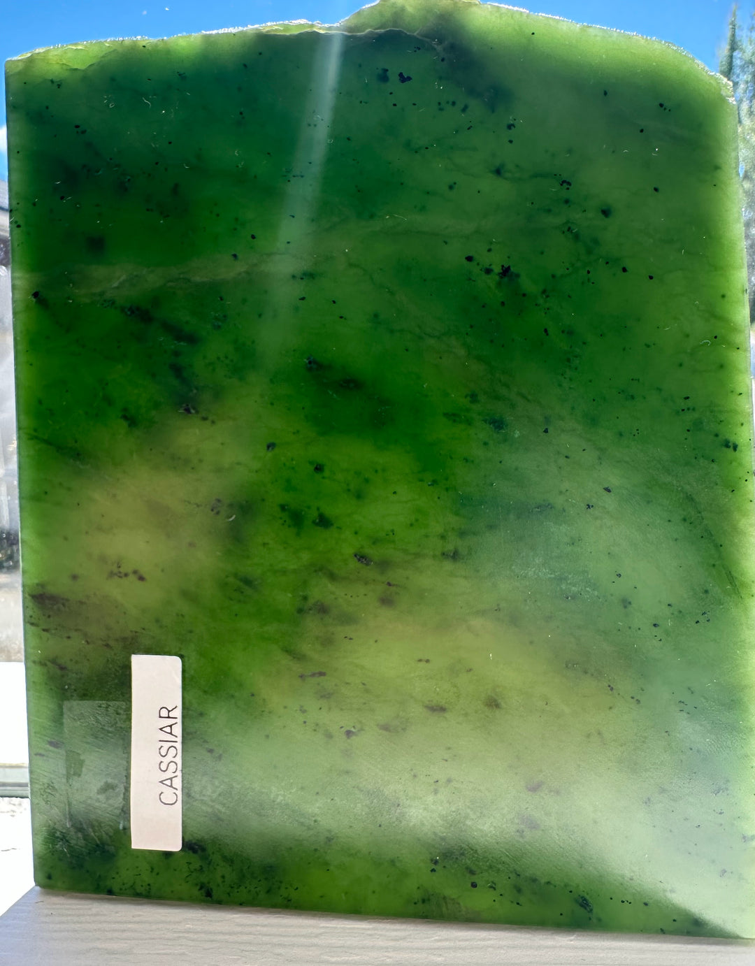 A Grade Canadian Jade Slab 240g shown outdoors with a blue sky, green jade, and a Cassiar label along the lower edge.