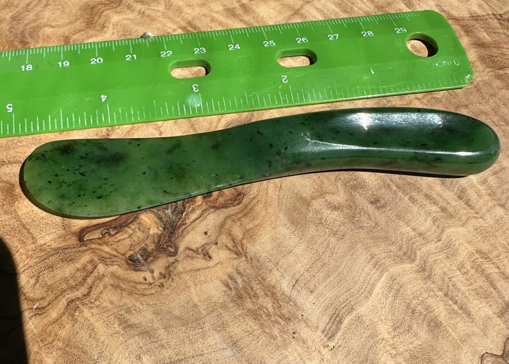 Green jade butter knife on a wooden surface with a green ruler for scale.