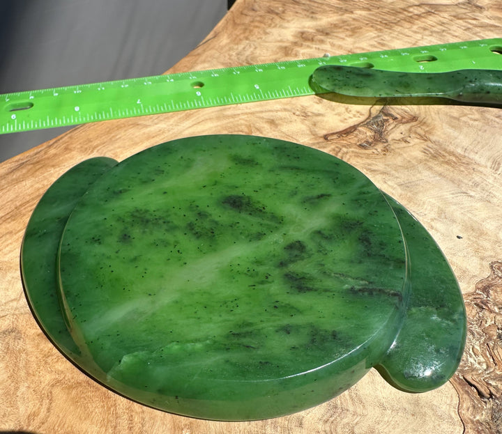 Green jade stone on a wooden surface with a green ruler for scale.