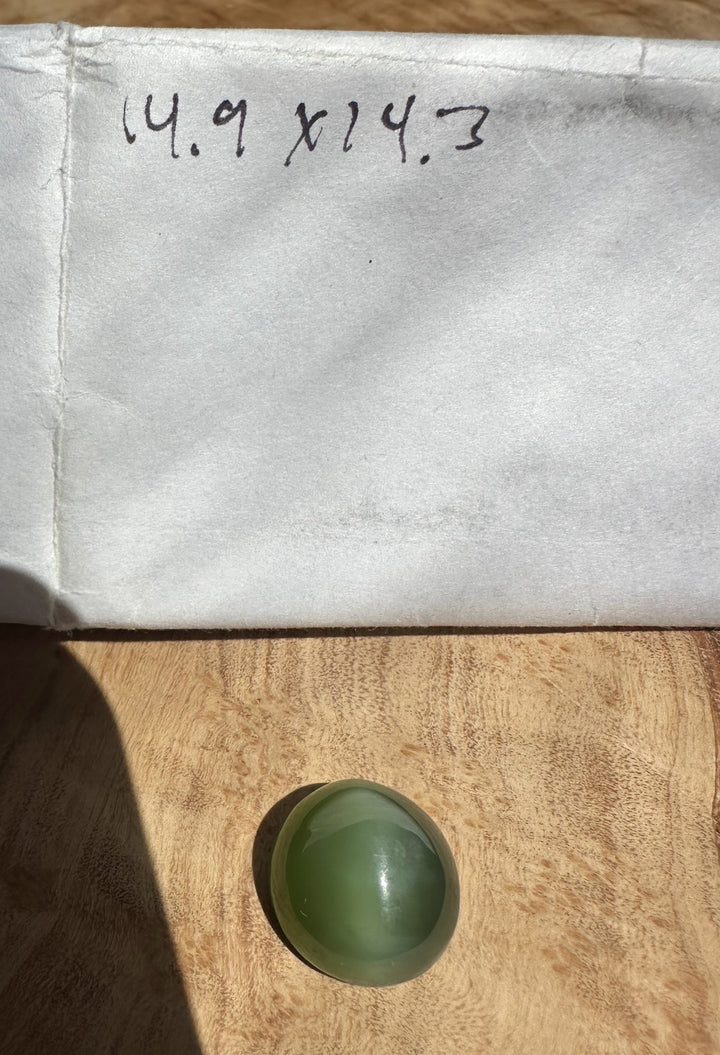 Green jade cats eye on a textured beige surface, with cabochon paper