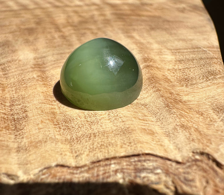 Siberian Cats Eye green cabochon with a domed surface on a wood background