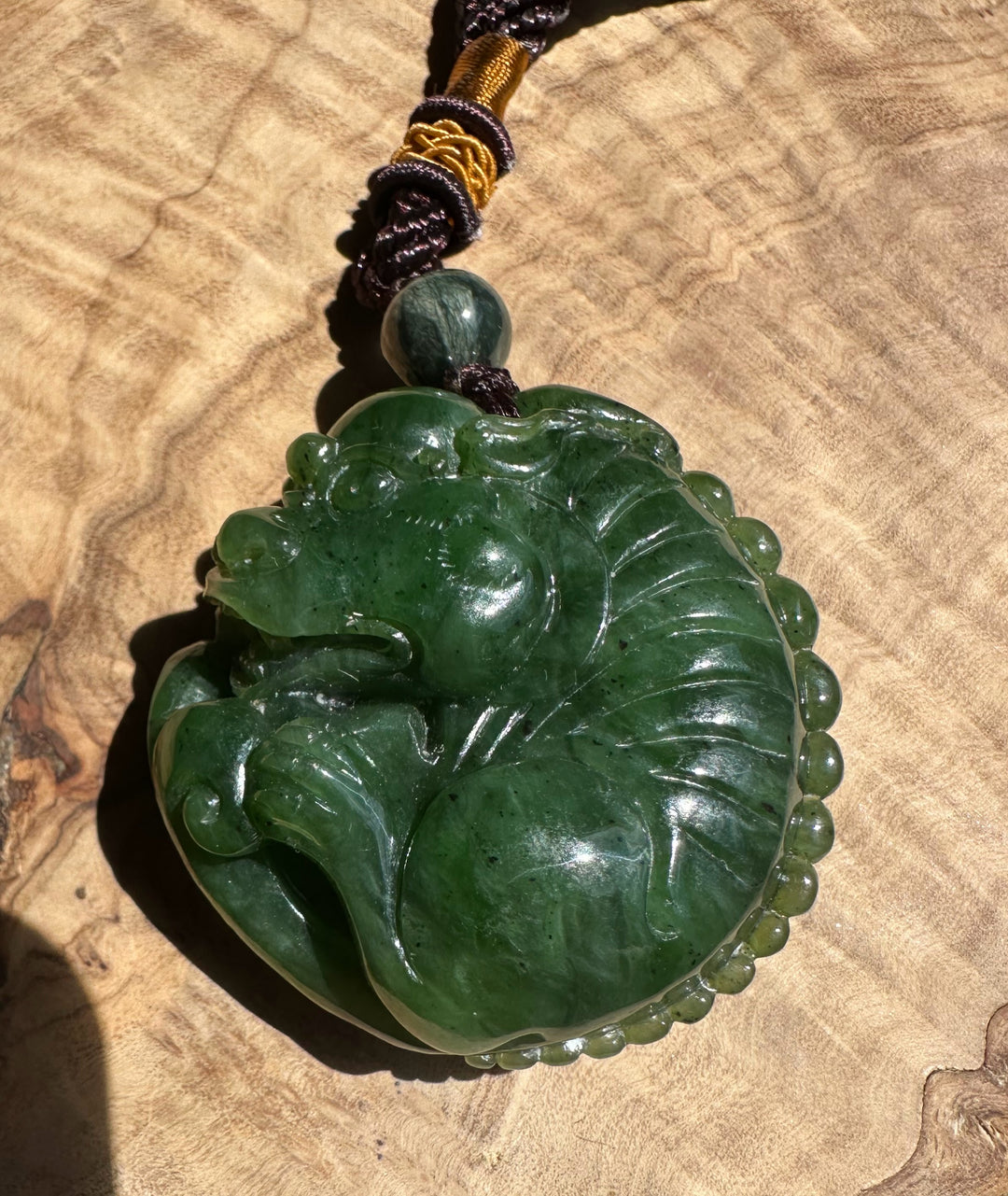 Canadian Jade Pocket Pendant Qi Lin with dark braided cord and a large green carved jade pendant against a tan surface