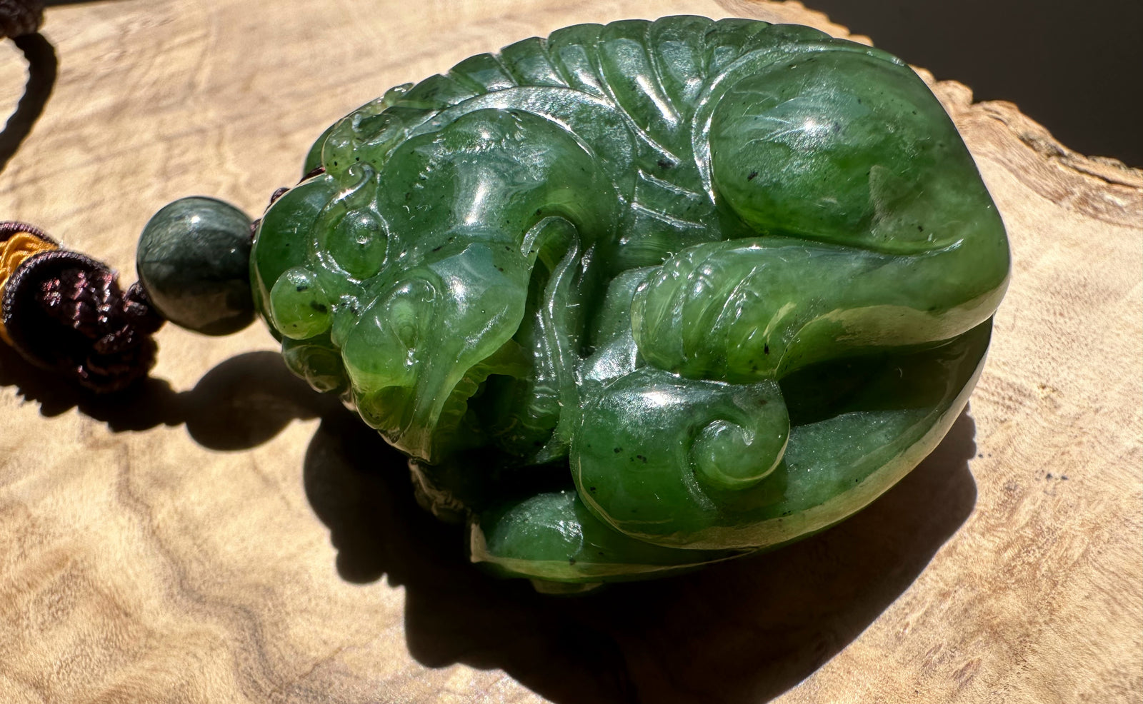 Canadian Jade Pocket Pendant Qi Lin shown on a light wood surface with round jade bead and carved green pendant